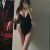 Woman in a black one-piece swimsuit posing for a mirror selfie, with a mural visible on the left in the room.