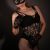 Woman in black lace lingerie, fishnet stockings, gloves, and a cat mask posing against a dark backdrop.